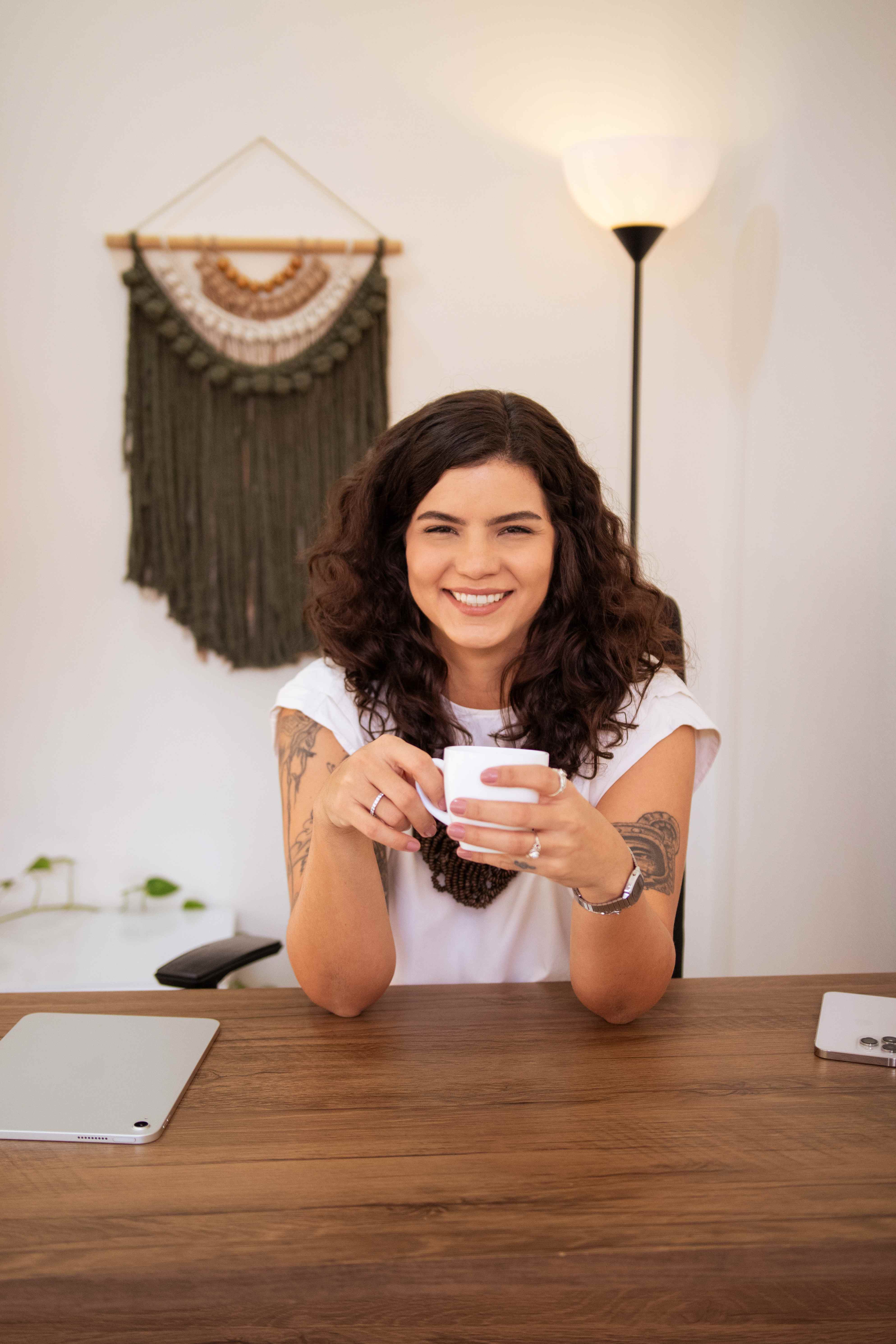 Caroline Leonel, psicóloga, sorrindo sentada à mesa com uma xícara de café